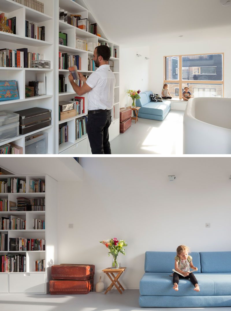 A bookcase that follows the line of the ceiling makes use of an otherwise plan white wall, while a couch helps to create a living room in the open space. #Bookshelf #InteriorDesign #LivingRoom