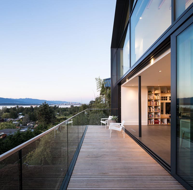 This modern living area has large sliding glass doors that open up to a balcony with a glass railing. #Balcony #Architecture