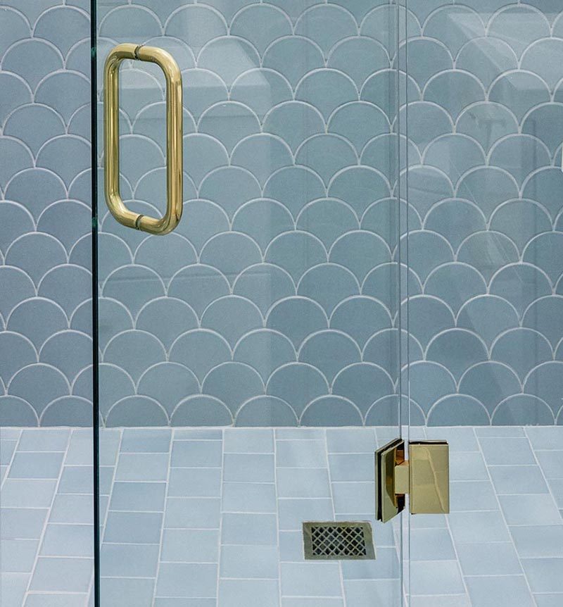 In this modern bathroom, In the shower, scalloped tiles (also known as fish scale tiles) that transition from white on the upper half of the shower, into blue tiles that line the lower half. Both the scalloped tiles wrap around the walls of the bathroom. #BathroomTiles #ModernBathroom #ScallopedTiles