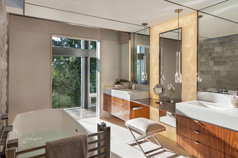 In this modern master bathroom, a makeup vanity lies between two bathroom vanities, while a freestanding bathtub is located on the opposite wall. #MasterBathroom #BathroomDesign