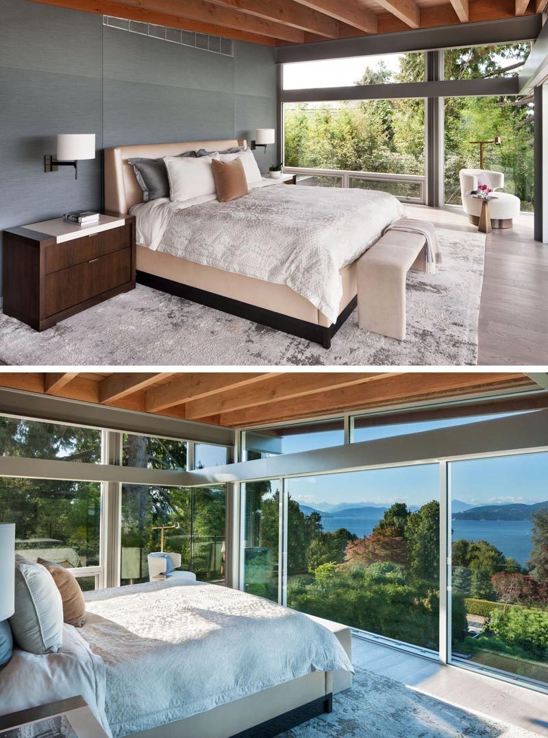 This modern master bedroom has a grey accent wall and windows that look out to the water and mountains in the distance. #MasterBedroom #Windows