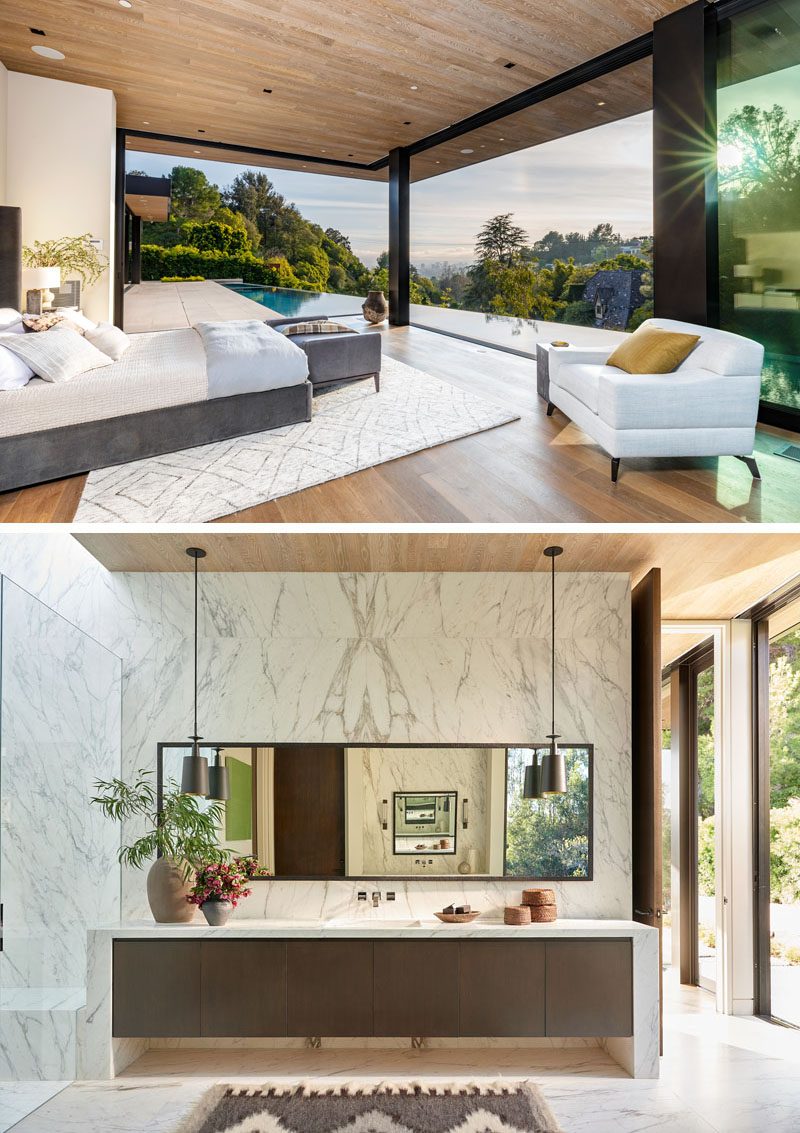 In this modern master bedroom, glass walls slide open to connect the bedroom with the outdoor patio and swimming pool. In the en-suite bathroom, grey and white marbled stone covers the wall and continues into the shower, while two pendant lights hang above the long vanity. #MasterBedroom #EnsuiteBathroom #GlassWalls #WoodCeiling