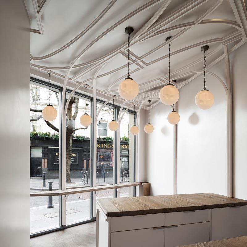 In this café, heavy-set mullions are halved and extruded from their frames to form ribbons that curve and fold over the ceiling in a style reminiscent of ornamental plasterwork. #Architecture #InteriorDesign #CafeDesign