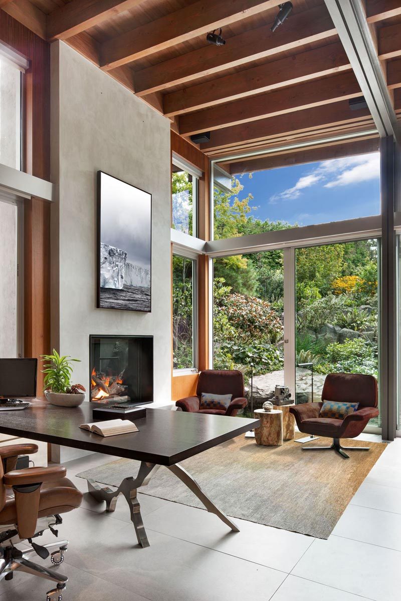 This modern den has high ceilings, a built-in fireplace, and a sliding door that opens to the garden. #ModernDen #ModernHomeOffice