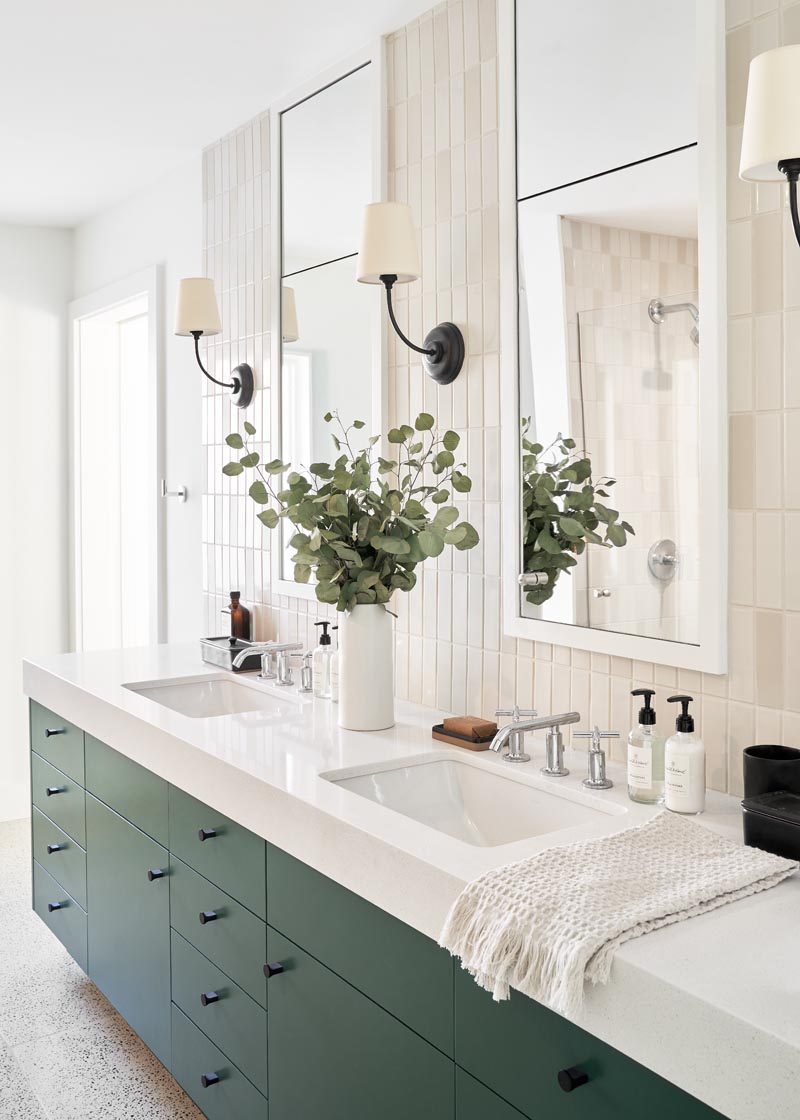 In this modern bathroom, there's a matte deep green vanity with dual sinks, while two vertical white-framed mirrors hang on a light colored tiled wall that also matches the tiles the shower. #ModernBathroom #GreenVanity #VanityIdeas #VerticalMirrors #TielsWalls