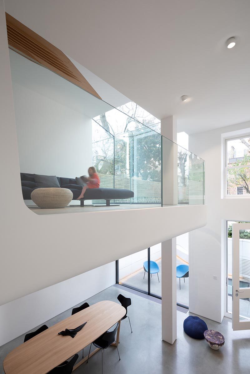 This modern house has a sitting room that opens up to a space with a couch with views of the garden and the lower level of the home. #GlassRailing #SittingRoom