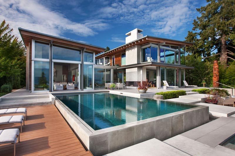 This northwest contemporary house has large windows, post and beam construction, a swimming pool with outdoor space, and a garden with a water feature. #ModernHouse #HouseDesign #Architecture #SwimmingPool