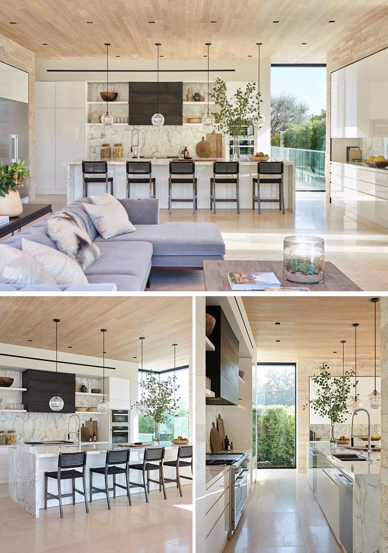 In the kitchen, a long kitchen island provides a place for five people to sit at, while four simple glass sphere pendant lights hang above it. #ModernKitchen #KitchenIsland #KitchenDesign