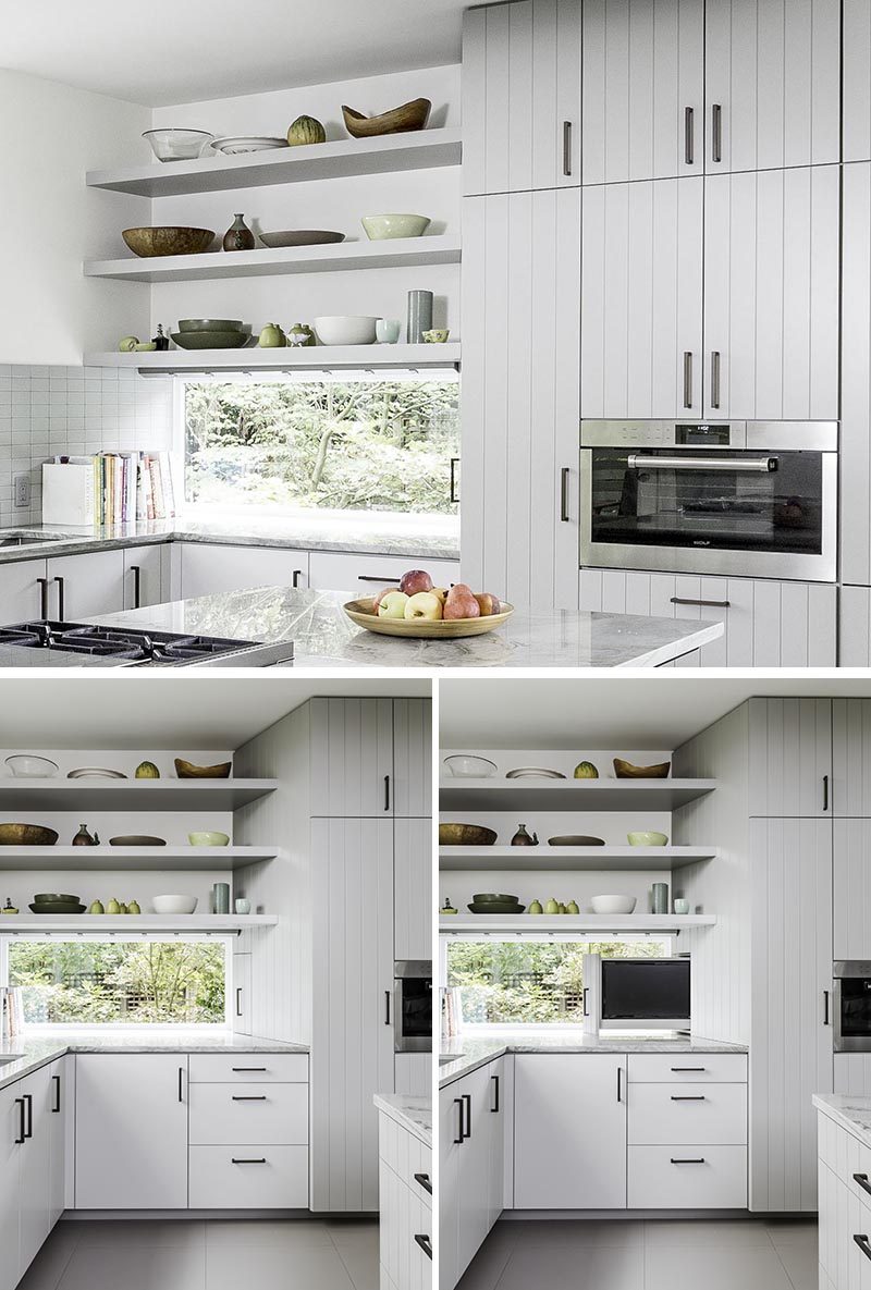 New windows add more light to this renovated kitchen, while open shelving shows off collected bowls and vases. Adjacent to the window is a unique television pullout shelf that allows the client to “put away” the kitchen TV when they want more counter space. A built-in oven at counter height is surrounded by cabinets that go from the floor to the ceiling. #ModernKitchenShelving #OpenShelving #KitchenDesign #ModernKitchen