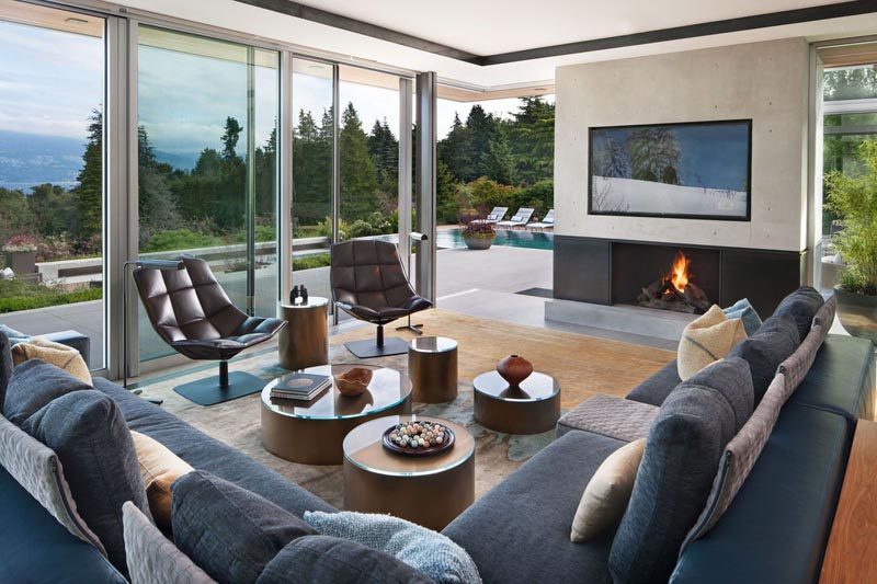 In this modern living space, floor to ceiling windows and doors open up to a patio that leads to the swimming pool. #LivingRoom #Fireplace