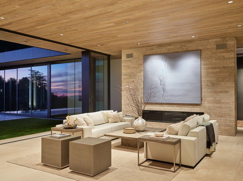 The social areas of this house include multiple living rooms. A neutral color palette has been used throughout the house, with the wood ceiling traveling from the interior to the exterior. #LivingRoom #Fireplace #GlassWalls #WoodCeiling