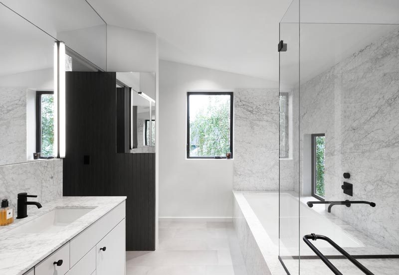 This modern master bathroom, which can be accessed from both the walk-through closet and the bedroom, has been clad in grey marble. A built-in bathtub and glass-enclosed shower line one wall of the bathroom, while the toilet is hidden from view behind a partition wall at the end. #MasterBathroom #EnsuiteBathroom #GreyBathroom #BathroomDesign #BuiltInBathtub