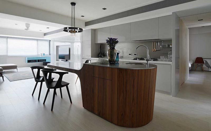 This modern multi-height kitchen island, which features a base that's been clad in vertical dark wood and a concrete countertop, has a small bar sink and food prep area at one end, and a cantilevered dining table at the other. #MultiHeightKitchenIsland #KitchenIslandDesign #CantileveredDiningTable #KitchenDesign #ModernKitchen #KitchenIslandIdeas