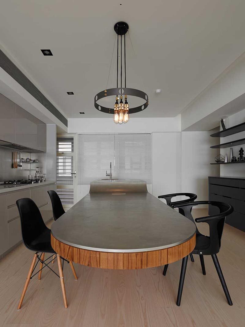 This modern multi-height kitchen island, which features a base that's been clad in vertical dark wood and a concrete countertop, has a small bar sink and food prep area at one end, and a cantilevered dining table at the other. #MultiHeightKitchenIsland #KitchenIslandDesign #CantileveredDiningTable #KitchenDesign #ModernKitchen #KitchenIslandIdeas