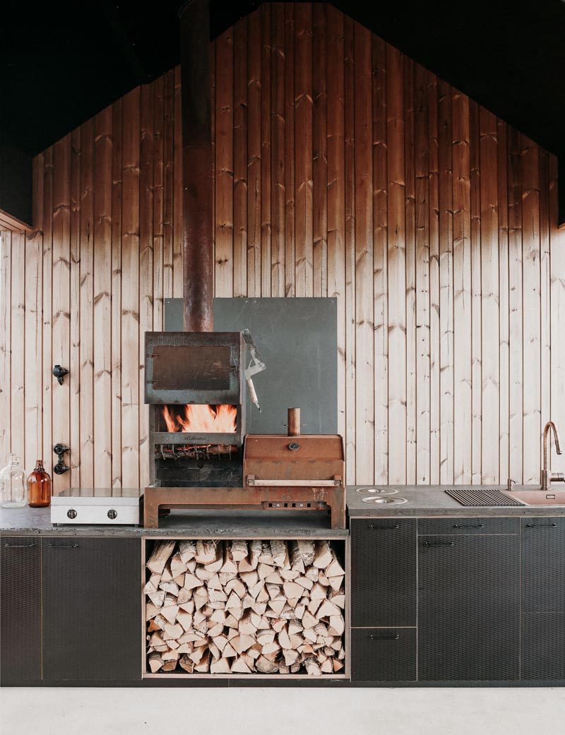 This outdoor kitchen has a row of black cabinets, a wood burning stove / bbq, and a sink. #OutdoorKitchen 