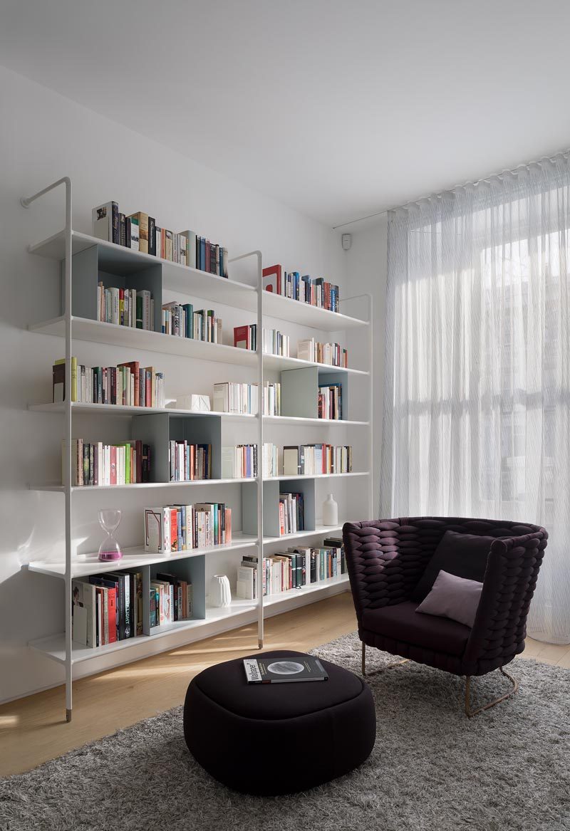 This modern sitting room features white open bookshelves and a comfortable armchair with matching footrest. #SittingRoom #Library #Shelving
