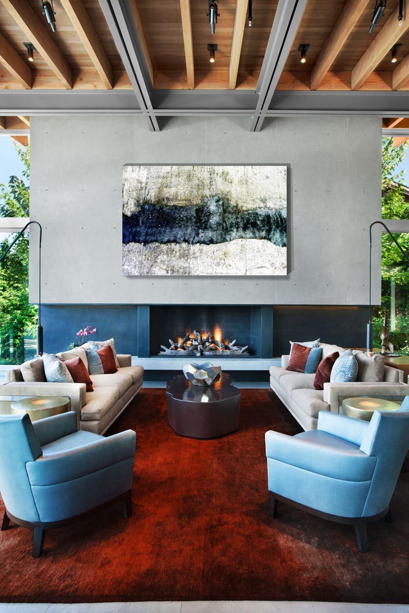 In this modern living room, a large abstract art piece hangs above the fireplace, while the exposed ceiling adds a natural element to the space. #LivingRoom #Fireplace