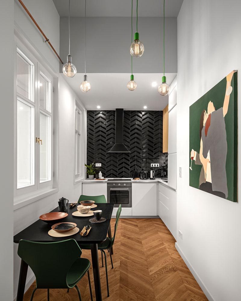 Gloss and matte black tiles have been used to create an accent wall in this modern kitchen, that features minimalist white cabinets and is complemented by the black dining table. #Kitchen #BlackTiles #WhiteCabinets