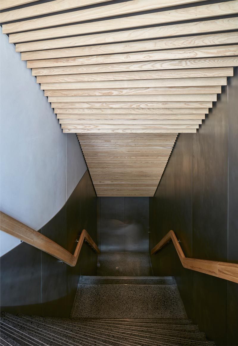Ash wood slats line the ceiling of these modern stairs in a restaurant. #WoodSlats #CeilingIdeas #ModernStairs