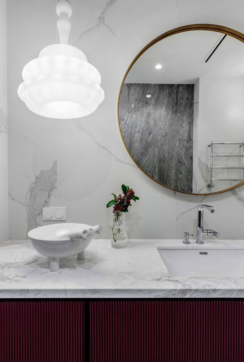 In this modern bathroom, grey marble covers the wall and vanity, while a Novecento suspension lamp from Vistosi hangs beside a circular mirror. #ModernBathroom #BathroomDesign #GreyBathroom