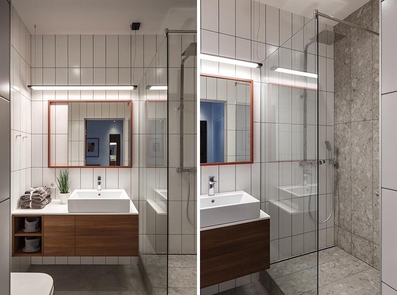 In this small bathroom, floor-to-ceiling rectangular tiles in a vertical arrangement cover the walls, while a wood vanity with a white countertop fits neatly beside the shower, that's separated by a glass screen. #SmallBathroom #WhiteTiles #BathroomDesign