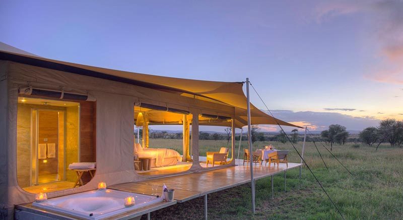 Raised up on a platform with wheels, this safari tent has an en-suite bathroom behind the sleeping area includes a flushing toilet, vanity basin and shower. The wrap around deck also features a sunken bath tub. #Serengeti #SafariCamp #SafariTent