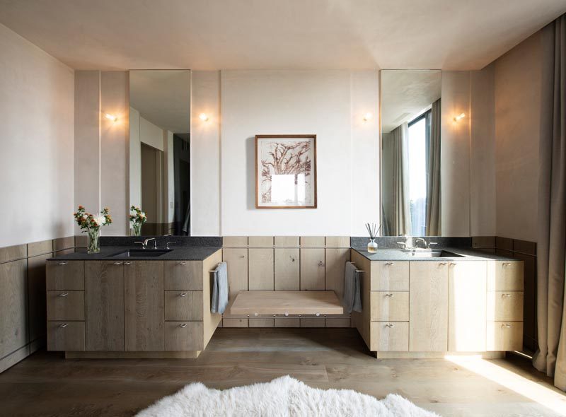 In this modern master bathroom, two wood vanities are separated by a small bench, while wood wainscoting has been used to add a unique design element to the space. #MasterBathroom #BathroomDesign