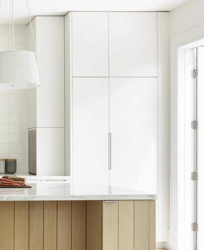 In this modern kitchen, minimalist white cabinets travel from the floor to the ceiling, while a small appliance garage is tucked away into one of the side panels. #WhiteCabinets #ModernKitchen #KitchenDesign #ApplianceGarage