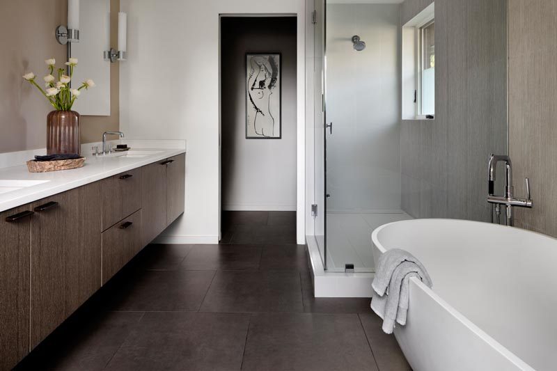 In this modern master bathroom, dark tiles contrast the light colored walls, the freestanding bathtub, and the white counters of the floating wood vanity. #ModernMasterBathroom #ModernBathroom #BathroomDesign