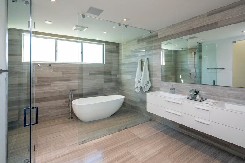 This modern master bathroom features a floating double-sink vanity, wood-like tile floors and walls, frosted doors, and a glass enclosed wet room that houses the shower and bath. #ModernBathroom #WetRoom #BathroomDesign #InteriorDesign #MasterBathroom