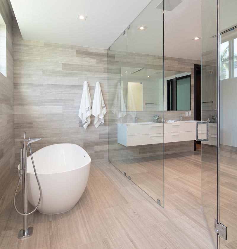 This modern master bathroom features a floating double-sink vanity, wood-like tile floors and walls, frosted doors, and a glass enclosed wet room that houses the shower and bath. #ModernBathroom #WetRoom #BathroomDesign #InteriorDesign #MasterBathroom