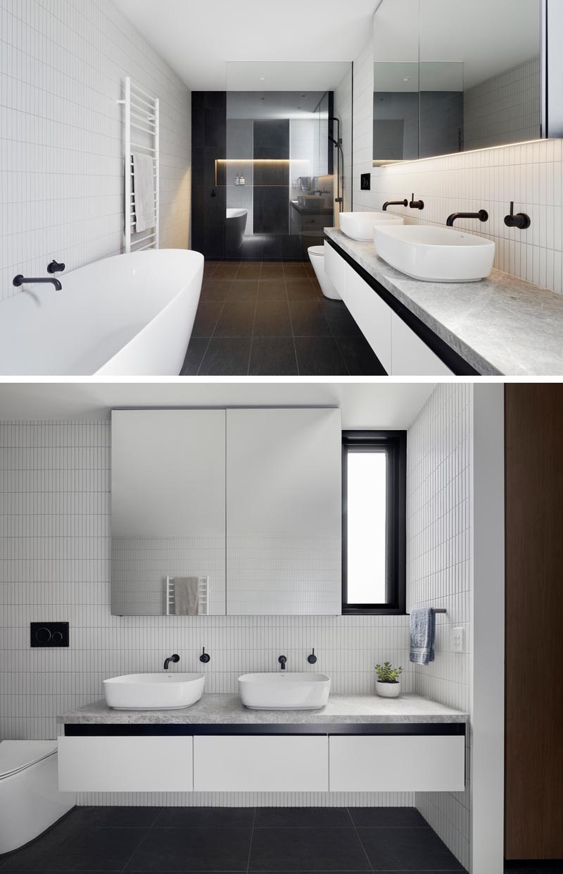 In the shower of this modern bathroom, black wall tiles are brightened by a shower niche with hidden lighting. A glass shower screen allows light to travel throughout the room. Contrasting the black tiles are the white tiles on the walls and other white accents like the bathtub, towel rack, vanity, and sinks. #ModernBathroom #BlackAndWhiteBathroom #BathroomDesign #BlackTiles #ShowerNiche