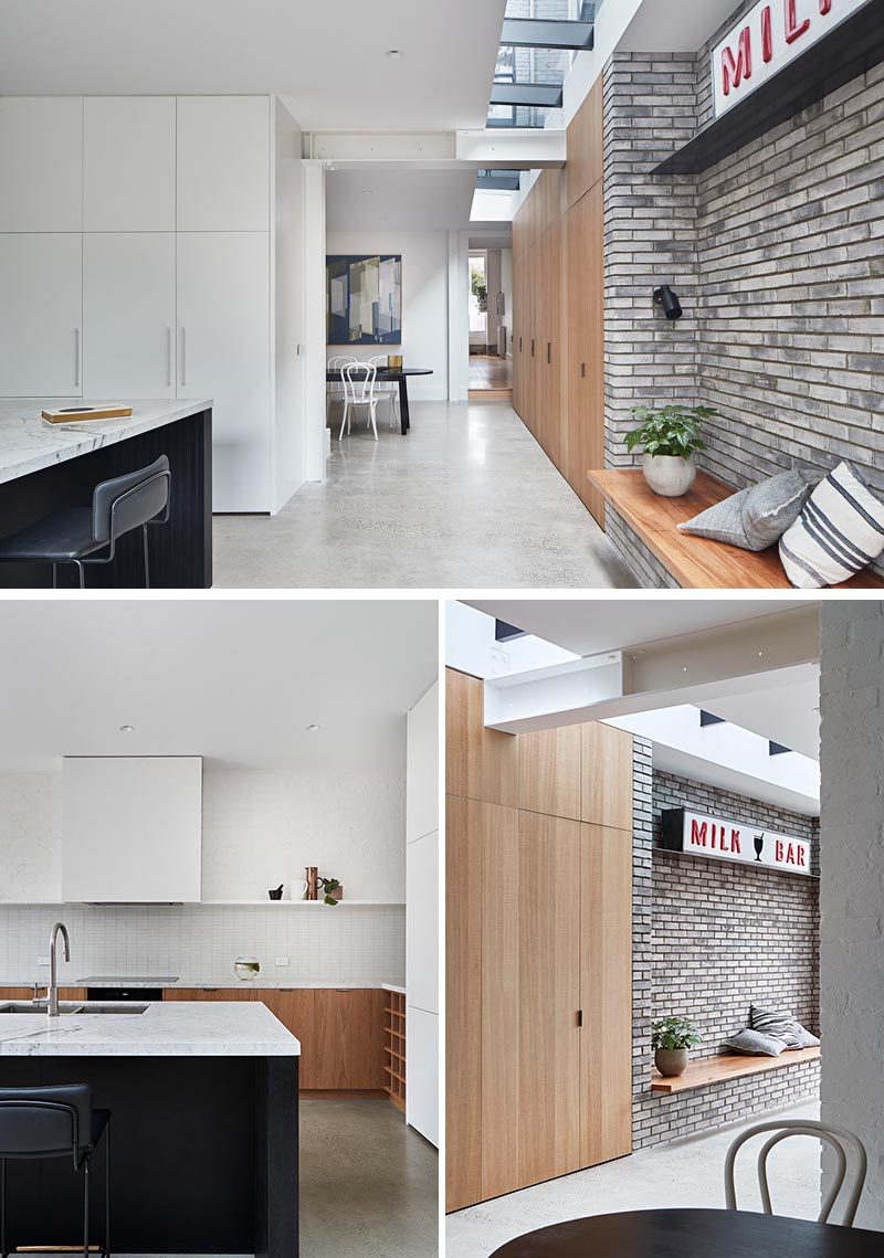 In this modern house extension, Polished concrete flooring complements the grey brick accent, while the  built-in wood bench sits opposite the kitchen. White and wood cabinets, a  black island, and light Carrara stone countertops have been combined to  create a modern and open kitchen. #ModernInterior #ConcreteFloors #ModernKitchen