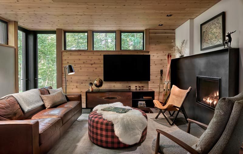 This modern living room has a black steel framed fireplace, while the wood ceiling wraps down onto the wall. #LivingRoom #BlackFramedFireplace #SteelFireplace