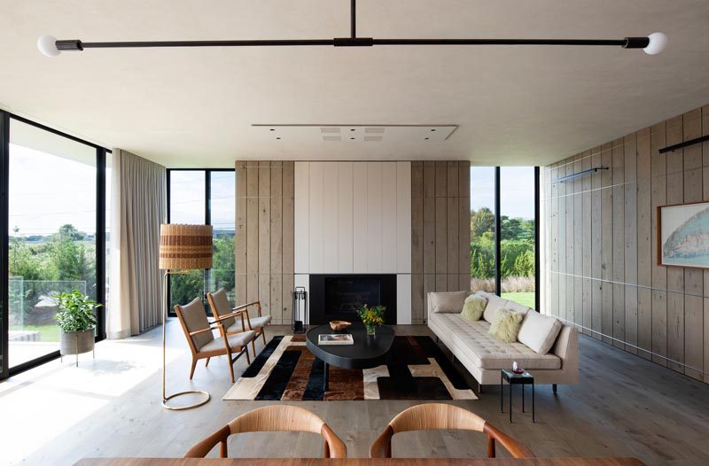 In this modern living room, wood clad walls surround the fireplace, while vertical windows on either side provide glimpses of the trees in the distance. #ModernLivingRoom #Fireplace #WoodWalls #InteriorDesign