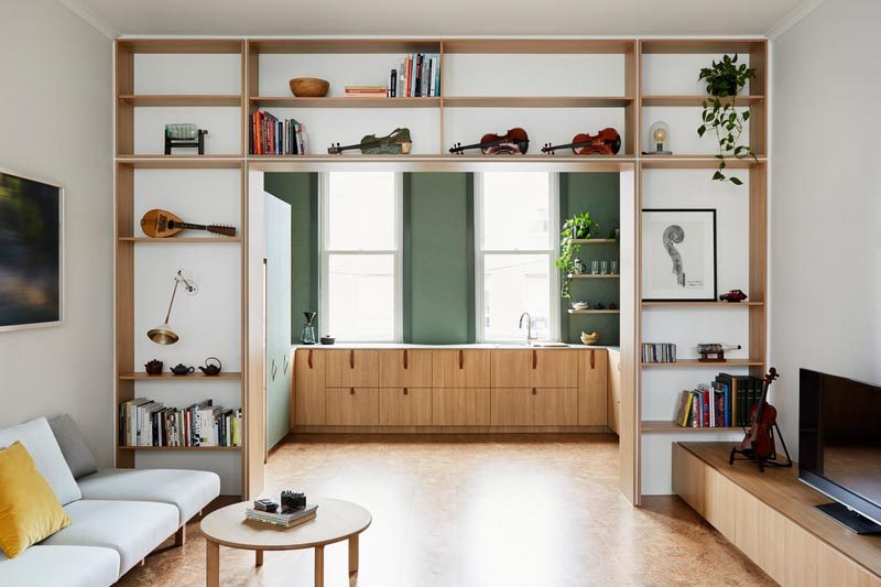This modern living room has custom built wood shelves that wrap around the open doorway to the kitchen, while cork flooring flows between both areas. #Shelving #CorkFlooring #LivingRoom #Kitchen