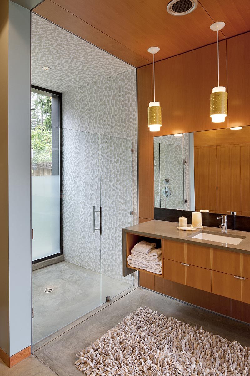 This modern bathroom has a number of design elements that work together to create a calming environment, with clear stained fir plywood adding a natural touch to the space. At one end of the bathroom is the shower, with a white and light grey mosaic tile shower, that even features tiles on the ceiling. #ShowerDesign #ModernShower #ModernBathroom