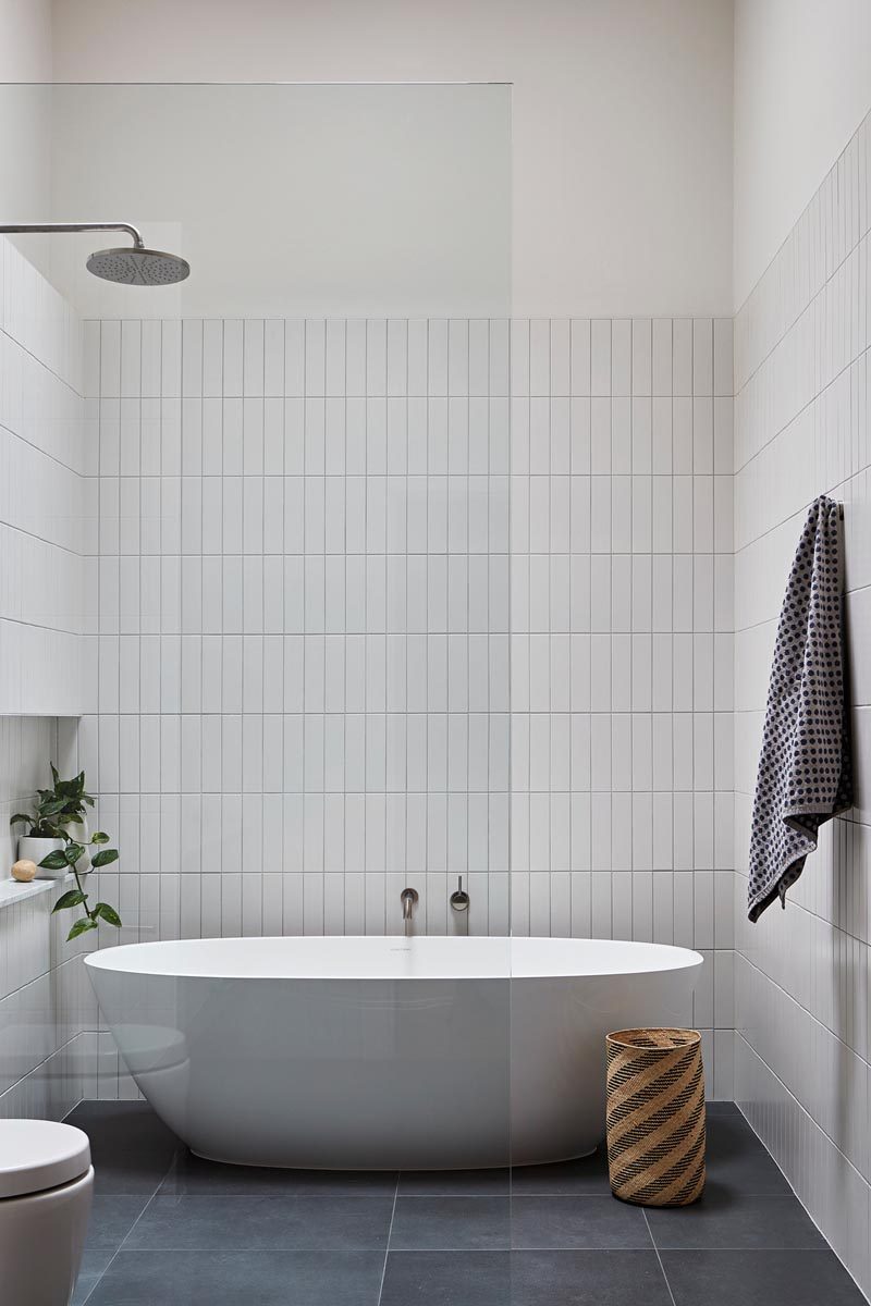 In this modern master bathroom, simple rectangular white tiles have been installed vertically, while Signorino stone tiles cover the floor. The freestanding bathtub shares the space with the shower, and a built-in niche creates a shelf for a plant and bathroom items. #ModernBathroom #BathroomDesign