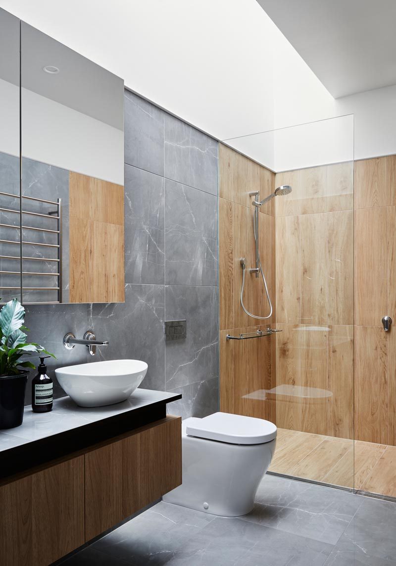 In this modern bathroom, a skylight brightens the space and highlights the wood-like tiles in the shower, and the grey tiles in the rest of the space. #BathroomDesign #ModernBathroom