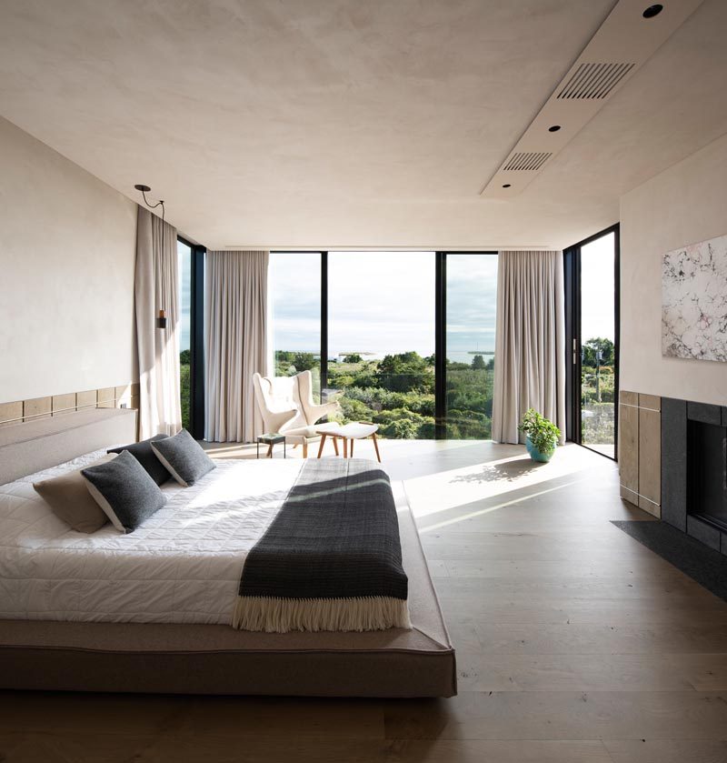 In this modern master bedroom, light colored walls, curtains, and furniture have been combined with wood elements and a fireplace to create a calming environment. #MasterBedroom #ModernBedroom #BedroomDesign