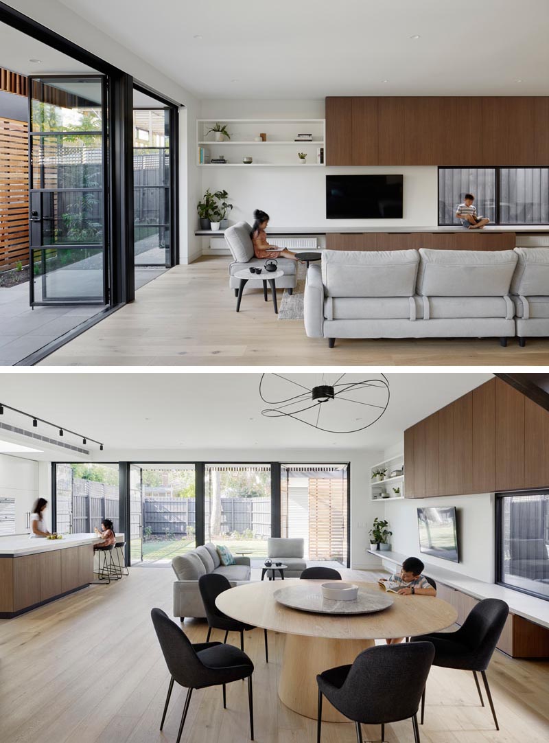 Steel frame glass doors open this modern extension to the backyard, and allow natural light to flood the interior. In the new living room, wood cabinetry and a bench line the wall, while light wood flooring helps to keep the space bright with a sense of warmth. #SteelDoors #GlassDoors #ModernLivingRoom