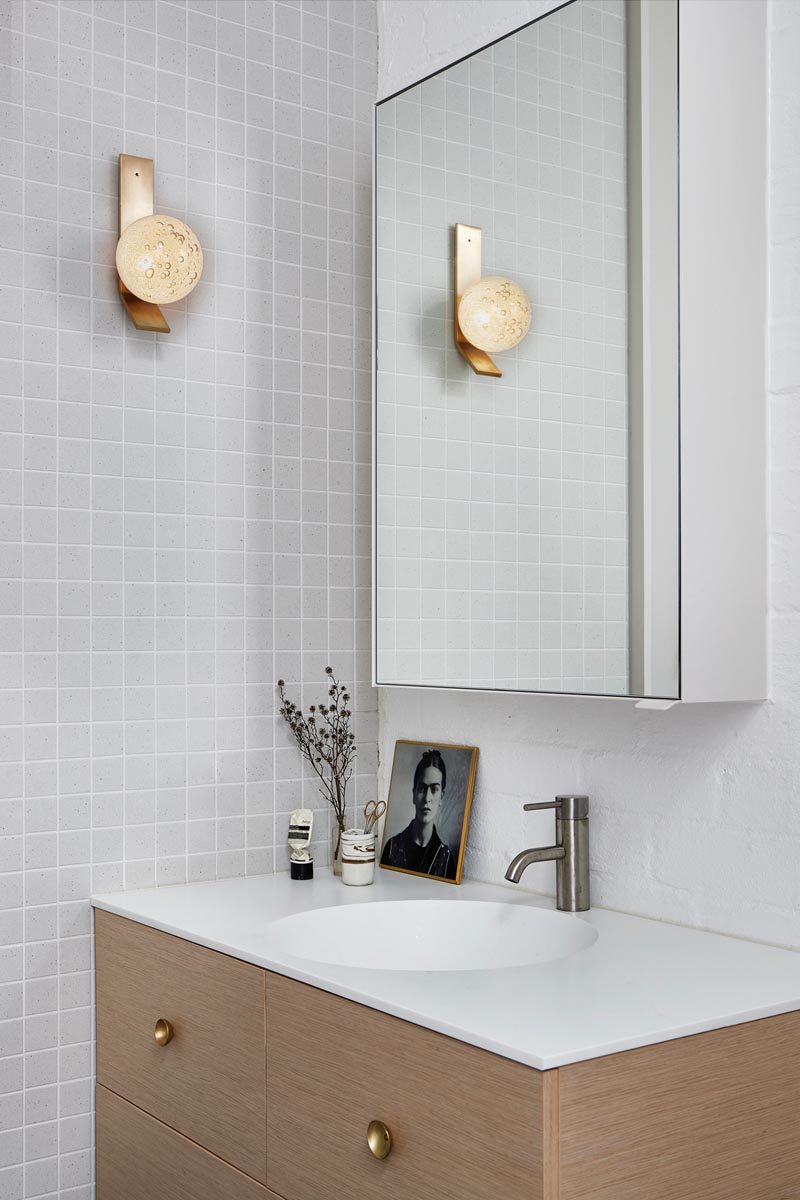 In this modern bathroom, simple grey square tiles cover the wall, while the wood vanity is topped with a white countertop that seamlessly flows into the sink. #ModernBathroom #LightGreyBathroom