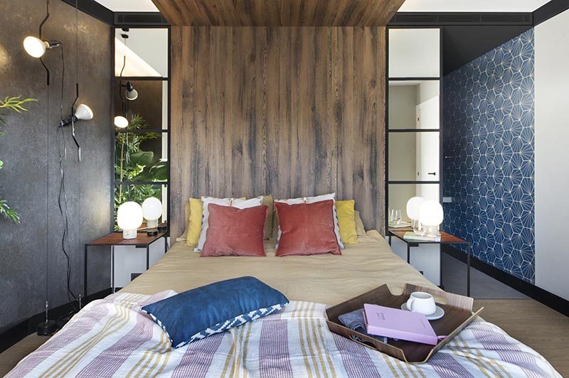 This modern bedroom has a wood headboard that wraps from the wall up onto the ceiling, and acts as an open wood canopy adding a natural touch to the room and defining an area for the bed. It also has hidden lighting that creates a soft glow and highlights the design element. #WoodHeadboard #WrapAroundHeadboard #ModernBedroom #BedroomDesign