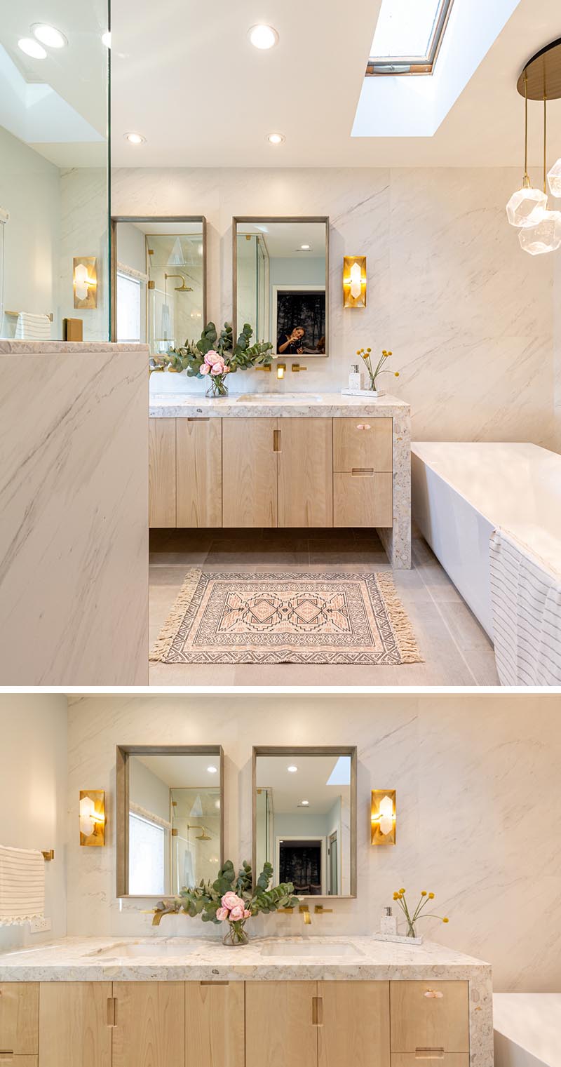 The soft color palette of this modern bathroom plays well with the floral and brass accents throughout. The wood vanity cabinets are hardware free, with just finger notches providing access to the storage within. #ModernBathroom #BathroomDesign #Skylight #Vanity