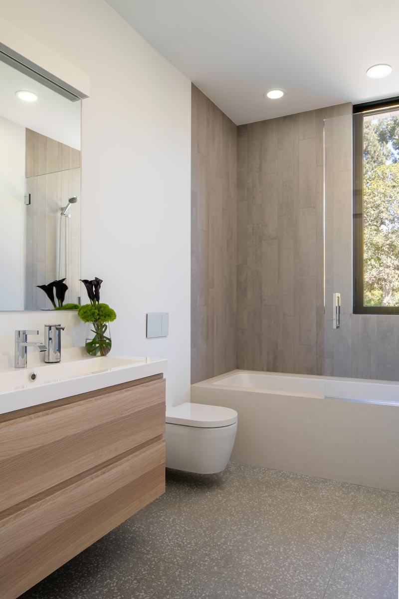 In this modern bathroom, a simple wood vanity has a white countertop, while tiles define the bath and shower. #BathroomDesign #ModernBathroom