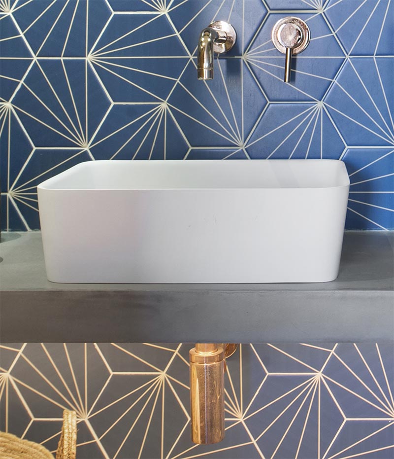 This modern blue bathroom has eye-catching starburst patterned tiles, rose gold tap and faucet, a concrete countertop, black and gold lighting, and a round mirror. #BlueBathroom #StarburstTile #ModernBathroom #BathroomIdeas