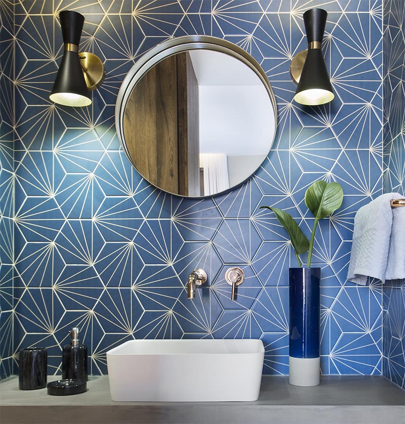 This modern blue bathroom has eye-catching starburst patterned tiles, rose gold tap and faucet, a concrete countertop, black and gold lighting, and a round mirror. #BlueBathroom #StarburstTile #ModernBathroom #BathroomIdeas