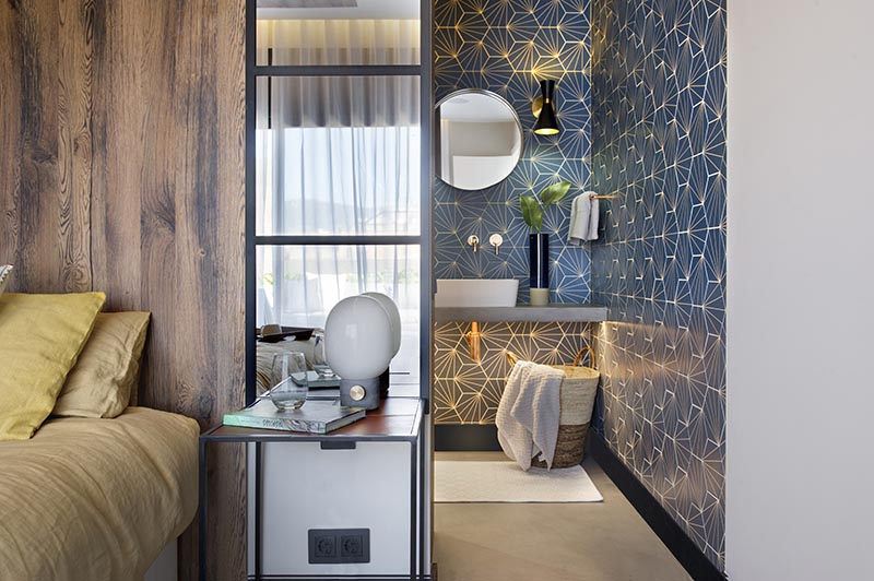 This modern blue bathroom has eye-catching starburst patterned tiles, rose gold tap and faucet, a concrete countertop, black and gold lighting, and a round mirror. #BlueBathroom #StarburstTile #ModernBathroom #BathroomIdeas