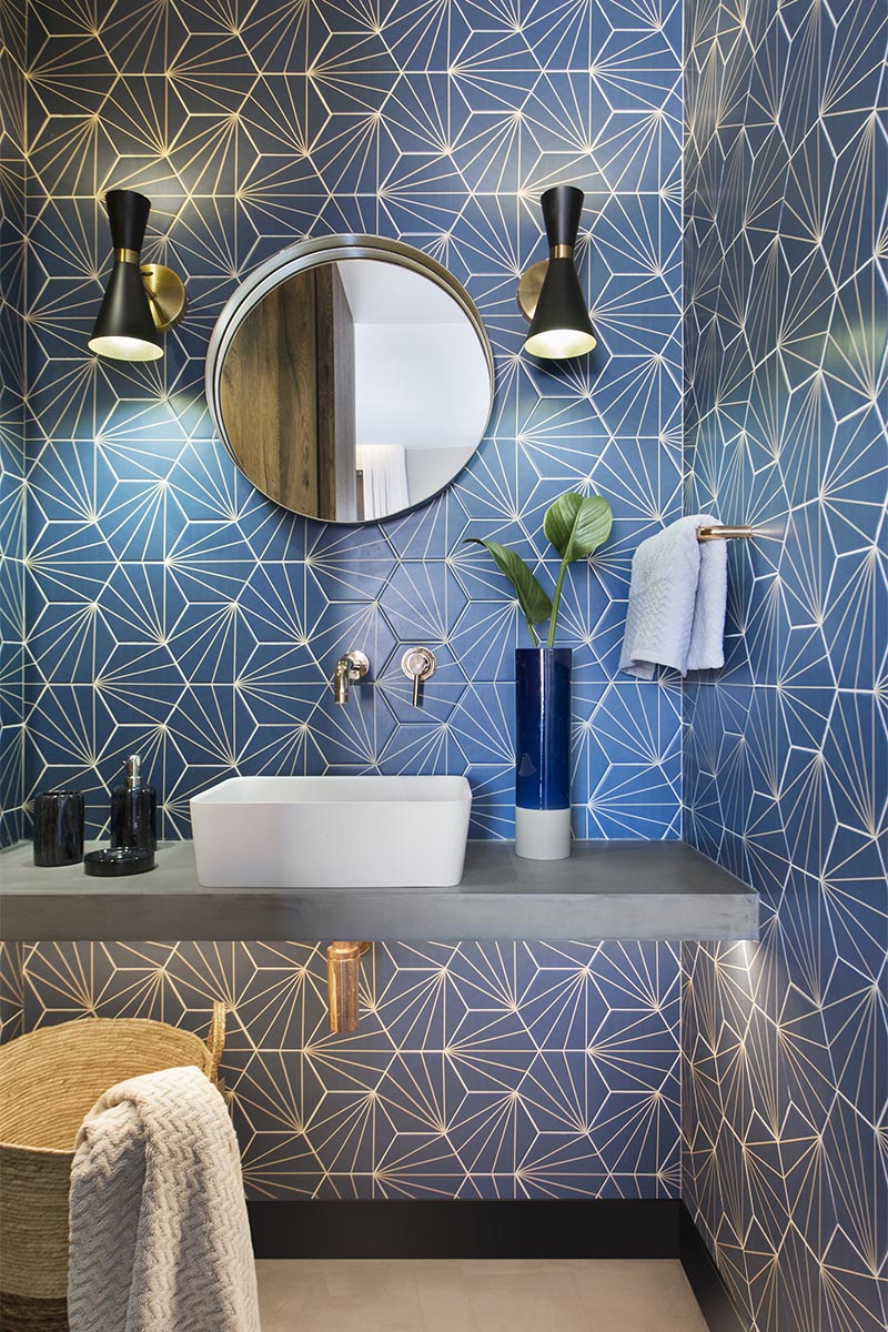 This modern blue bathroom has eye-catching starburst patterned tiles, rose gold tap and faucet, a concrete countertop, black and gold lighting, and a round mirror. #BlueBathroom #StarburstTile #ModernBathroom #BathroomIdeas