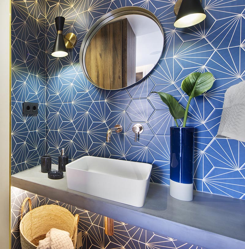 This modern blue bathroom has eye-catching starburst patterned tiles, rose gold tap and faucet, a concrete countertop, black and gold lighting, and a round mirror. #BlueBathroom #StarburstTile #ModernBathroom #BathroomIdeas